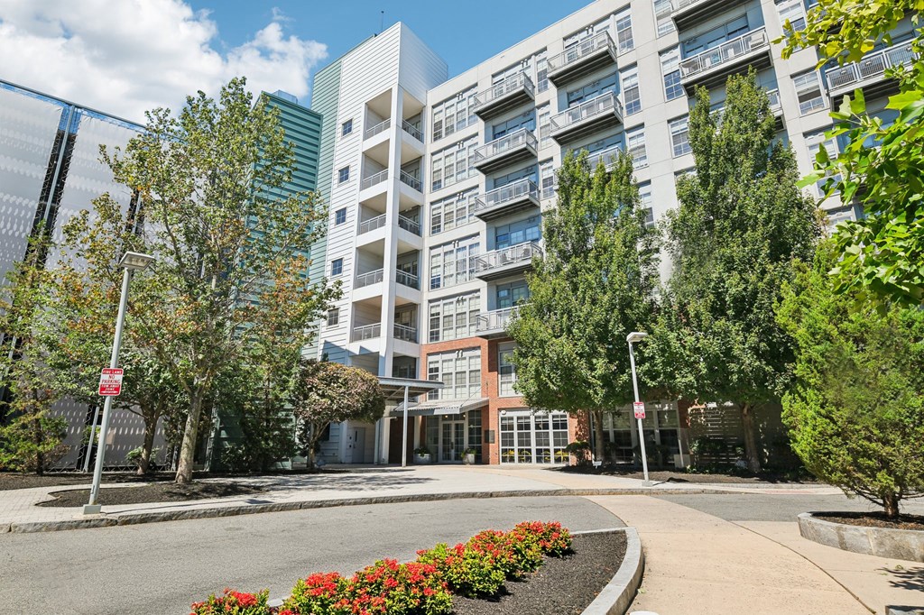 A modern building with a glass facade is surrounded by trees and flowers.
