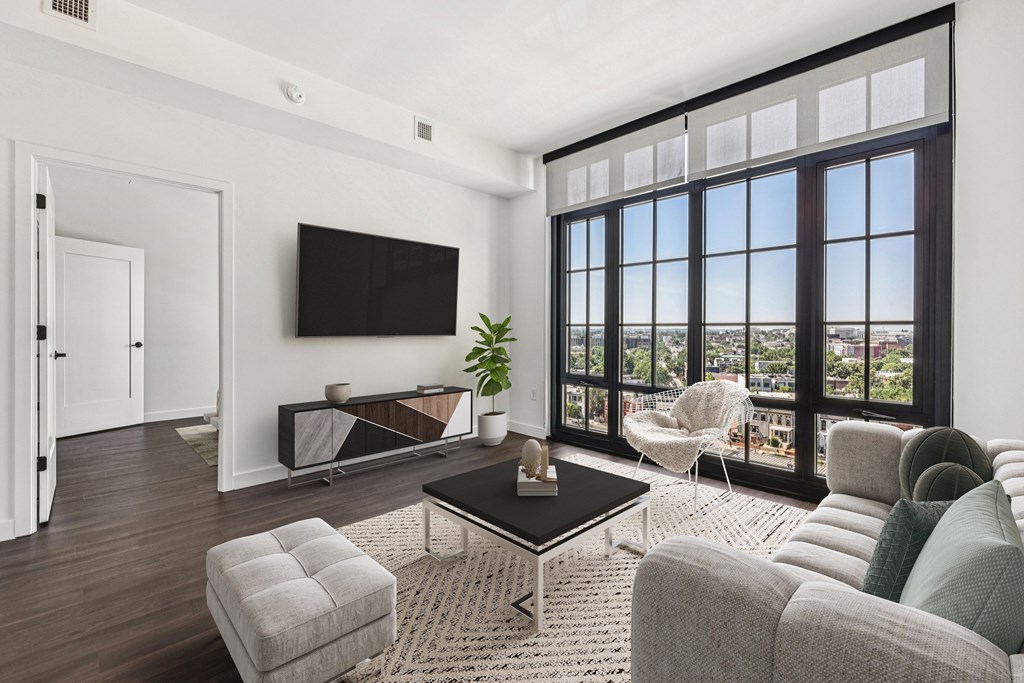 A living room with a flat screen TV mounted on the wall and a large window with a view of the city.