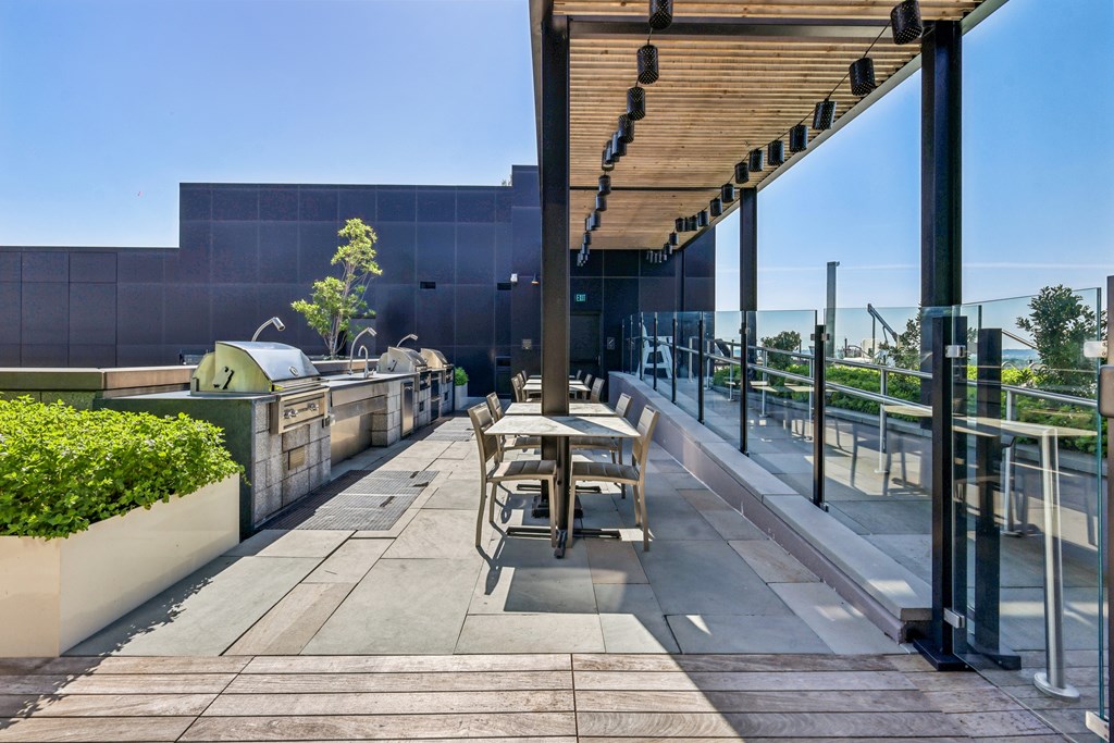 A modern outdoor seating area with a glass railing and a wooden pergola.