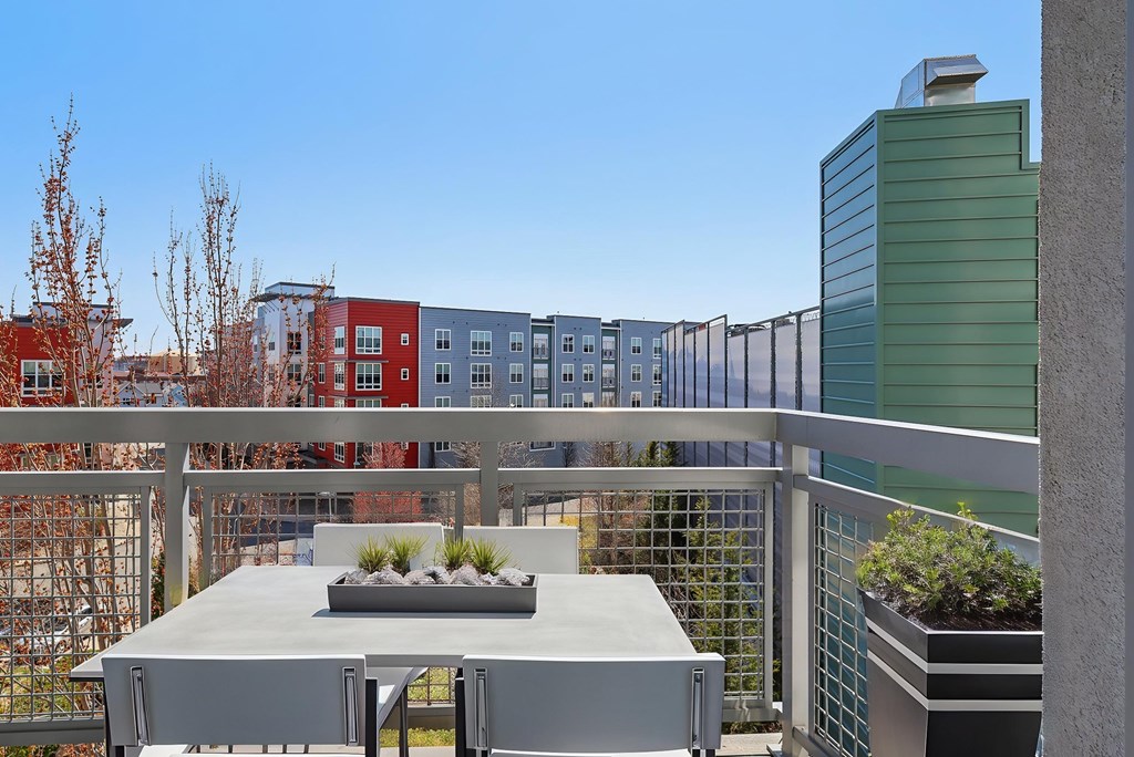 A modern balcony with a table and chairs overlooking a row of colorful buildings.