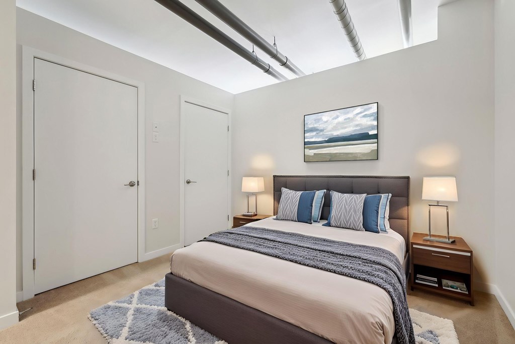 A bedroom with a bed, two lamps, and a painting on the wall.