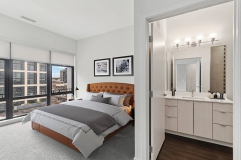 A bedroom with a large bed and a bathroom with a vanity and mirror.