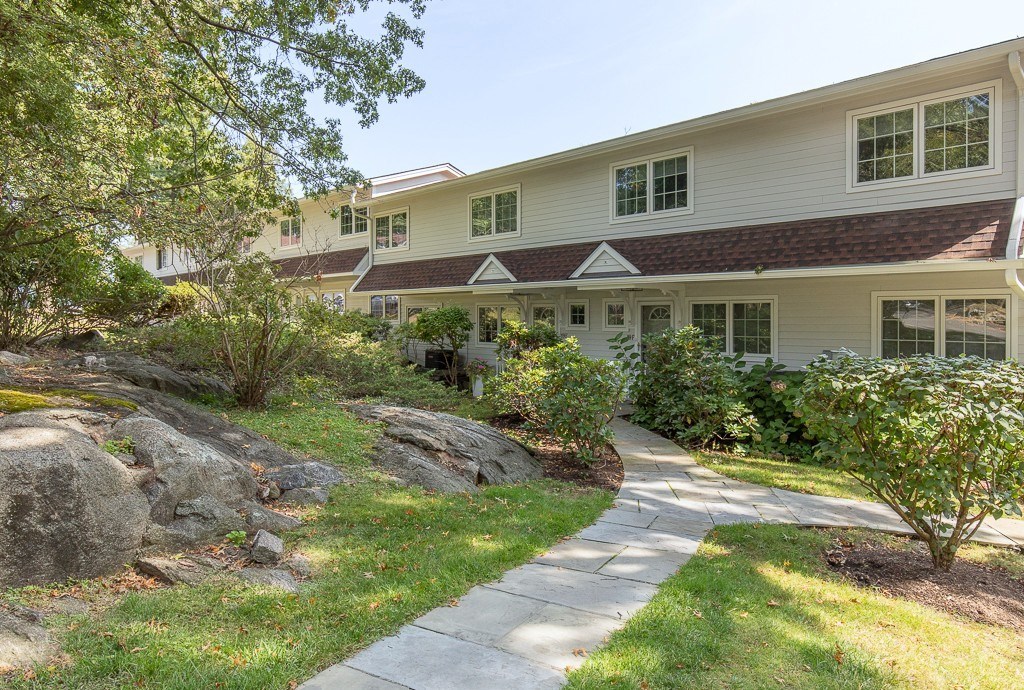 A residential building with a white siding and a brown roof is surrounded by greenery and a stone pathway.
