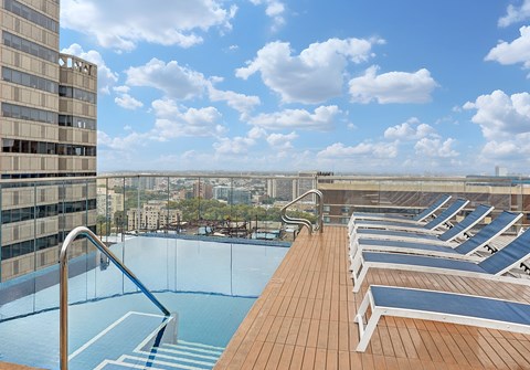 A rooftop pool with lounge chairs and a view of the city.