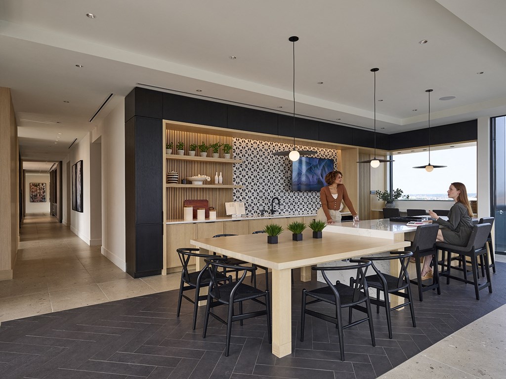 a rendering of a communal area with a table and chairs and two women working in the background