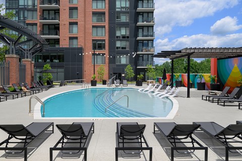 A pool surrounded by black chairs and a building in the background.