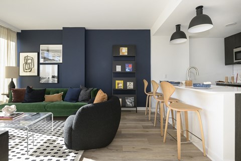 a living room with a green sofa and a kitchen with a bar and stools