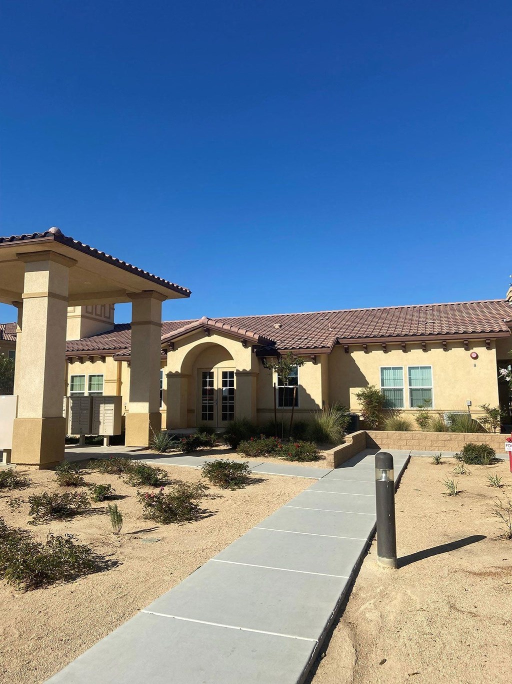 A building with a red tile roof and a covered walkway in front. A building with a red tile roof and a covered walkway in front.at The Villas 55+ II Hesperia, Hesperia, CA 92660