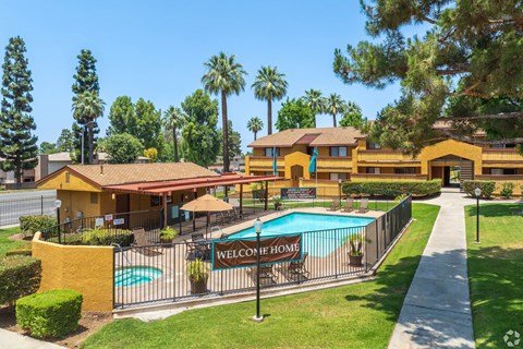 A yellow building with a pool in front and a sign that says "Welcome Home".
