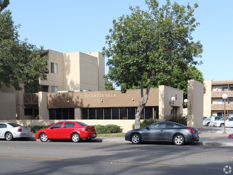 A red car is parked in front of a building with a sign that reads "Rosswood Village.".