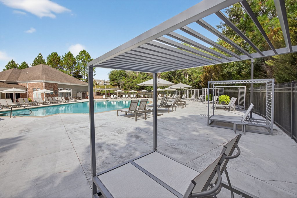 A pool area with a white pergola and several lounge chairs.