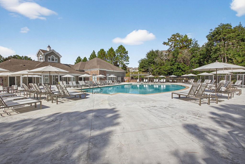 A large outdoor swimming pool surrounded by sun loungers and umbrellas.