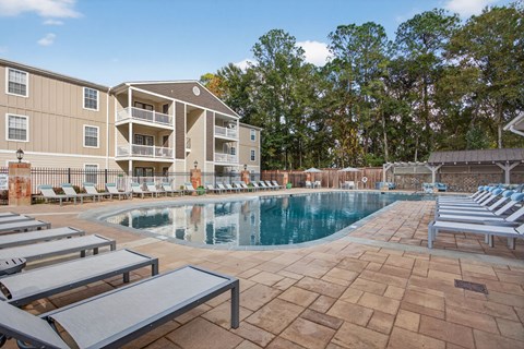 A large swimming pool surrounded by lounge chairs and a building in the background.