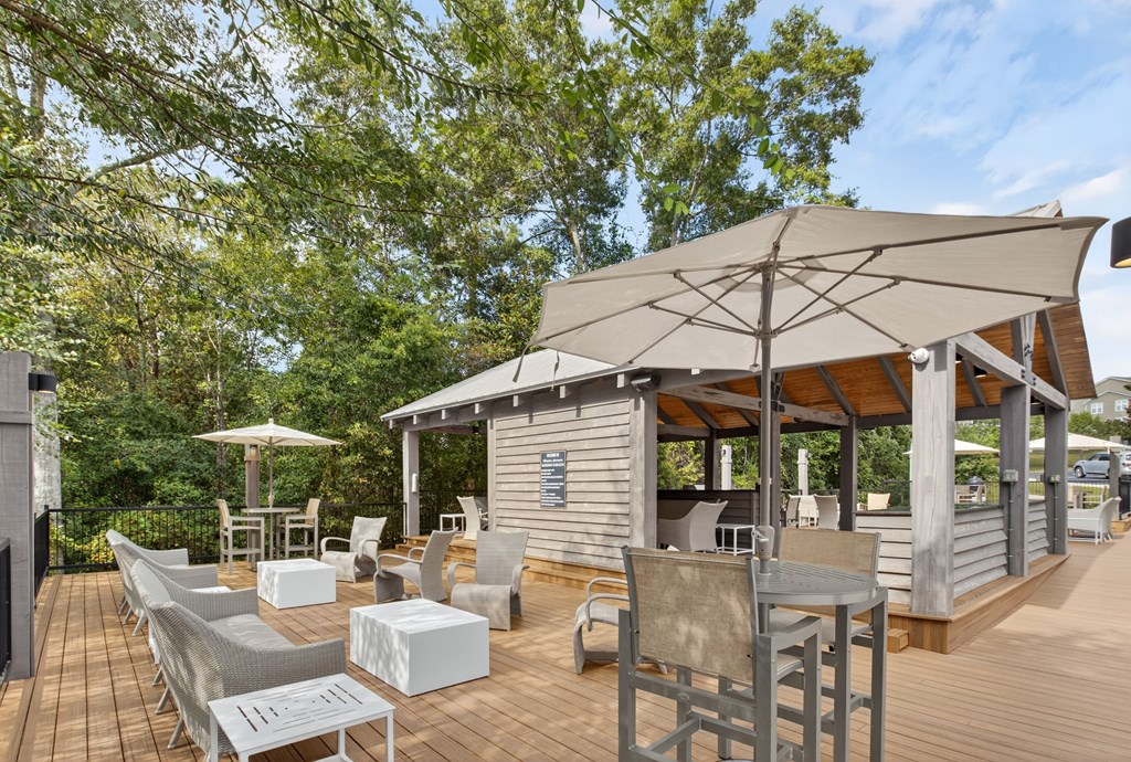 A wooden deck with chairs and a table under a large umbrella.