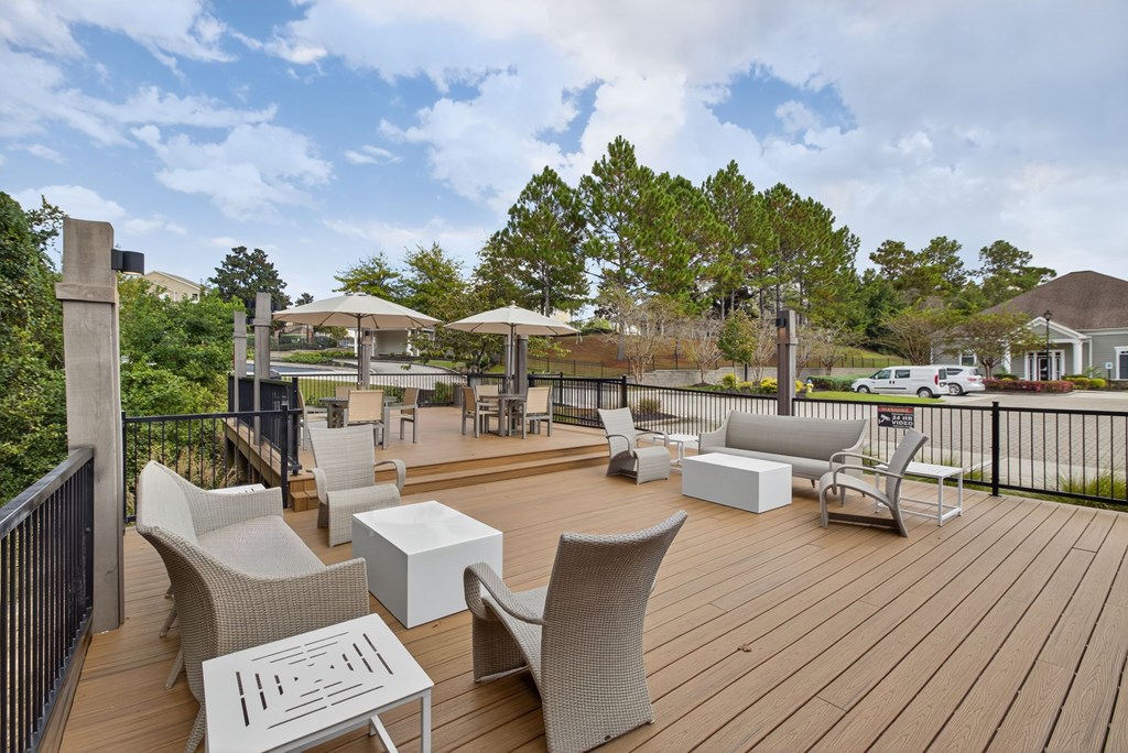A wooden deck with chairs and tables is surrounded by a black railing.