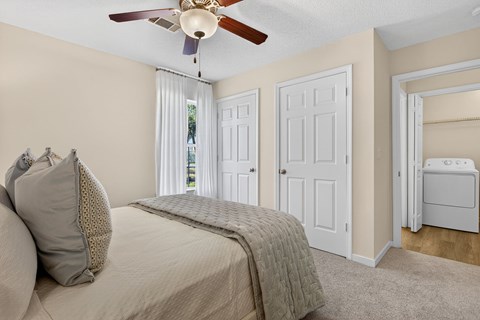 A bedroom with a bed, a ceiling fan, and a small refrigerator.