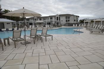 A pool area with chairs and umbrellas in front of a building at The Azul Apartment Homes in MS 38655