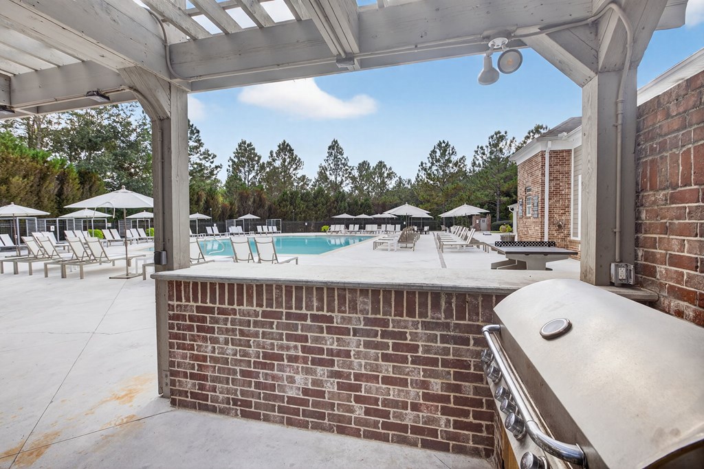 A pool area with a brick wall and a white pergola.