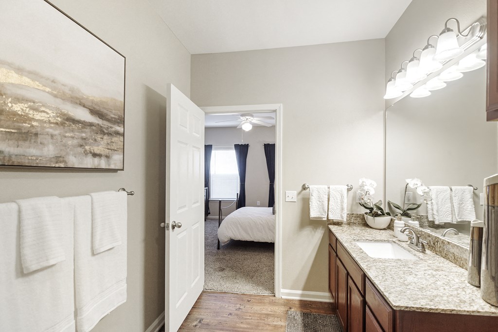 a bathroom with a mirror and a sink and a door to a bedroom at Cumberland Place Apartment Homes, Tyler, TX