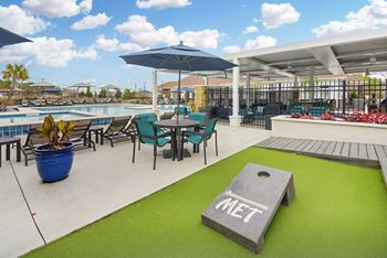 a patio with tables and chairs and a pool with umbrellas at The Met Apartment Homes in Hattiesburg, MS 39402
