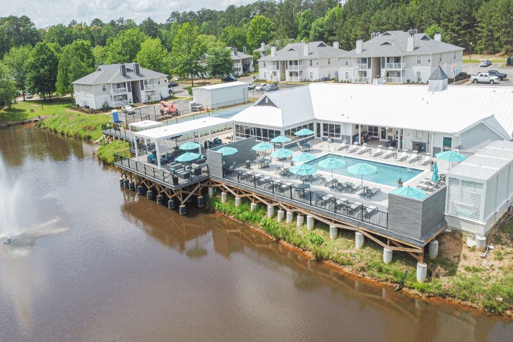 an aerial view of a resort with a swimming pool and patio next to a body of water at The Woodlands Apartment Homes, Meridian, MS