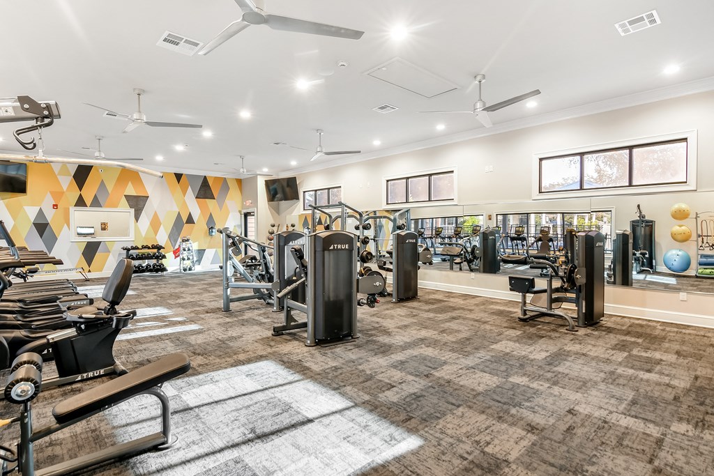 a gym with cardio machines and weights on a carpeted floor at Crossgates Apartment Homes, Starkville, Mississippi