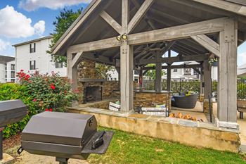 A wooden gazebo with a grill and a fire pit in the middle of a grassy area at Avalon Apartment Homes in MS 39759