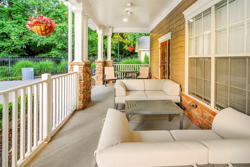 A white sofa and table are on a porch with a red flower hanging from the ceiling.