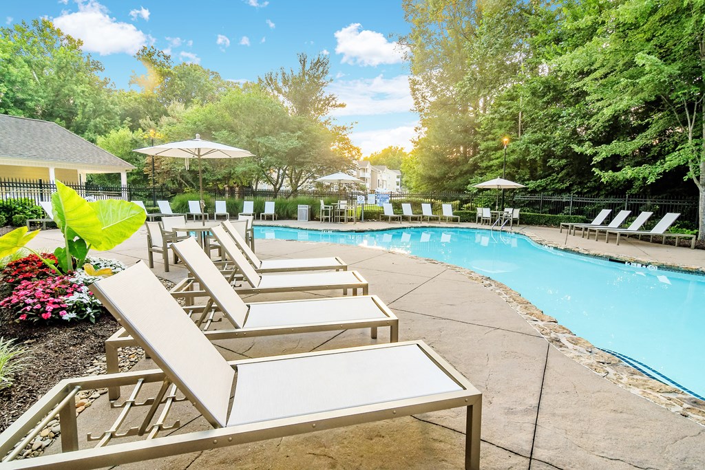 A pool surrounded by trees and chairs.