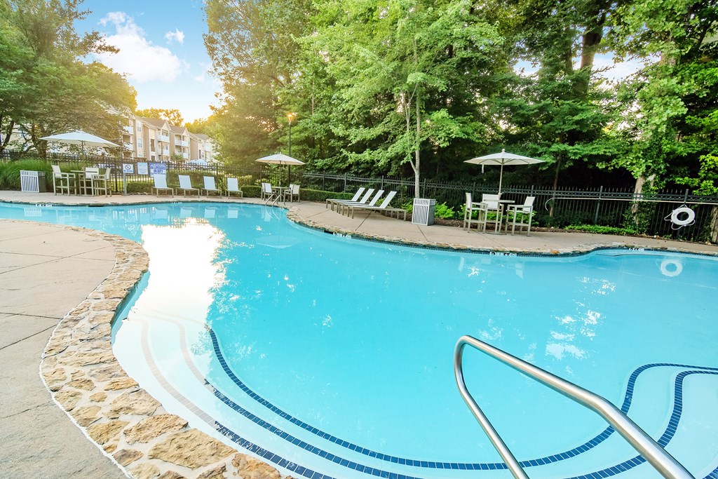 A swimming pool surrounded by trees and chairs.