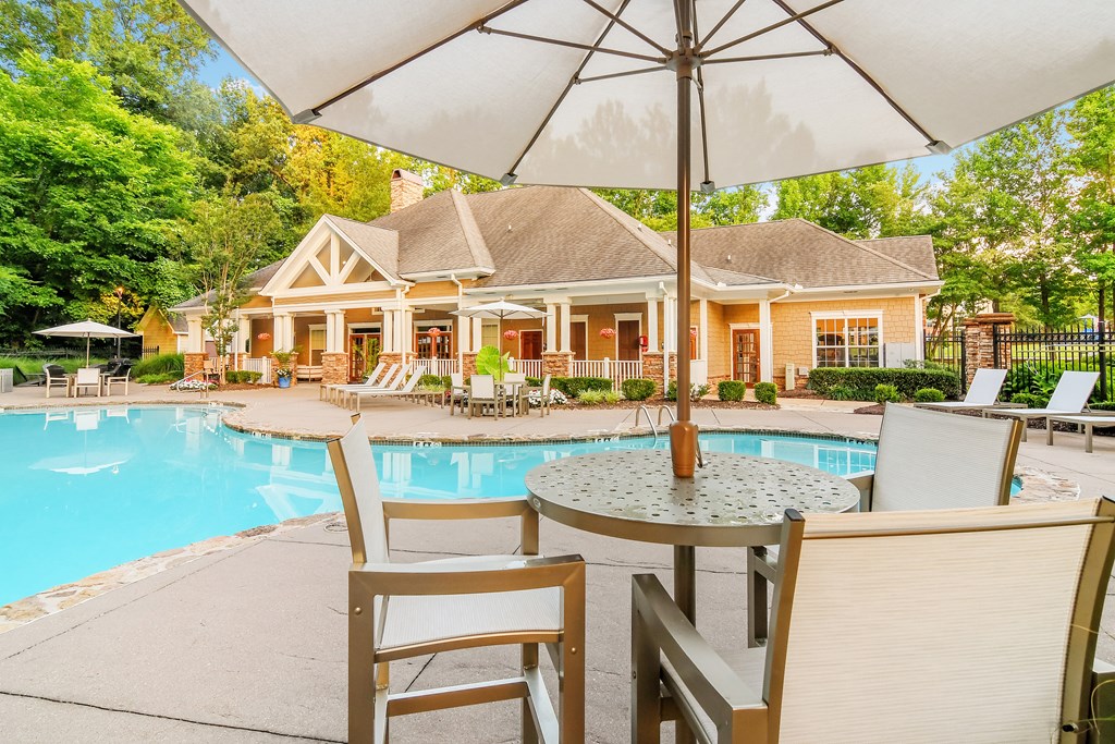 A poolside table with chairs and an umbrella in front of a house.