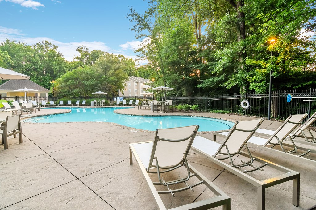 A pool surrounded by trees and chairs.