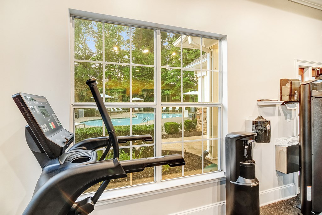 A treadmill is in a room with a window overlooking a pool.