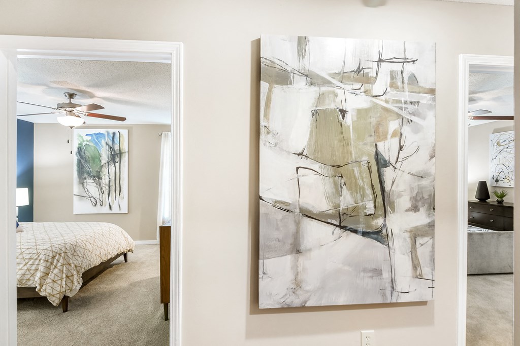 a living room with a painting and a bedroom with a bed at Crossgates Apartment Homes, Starkville, Mississippi