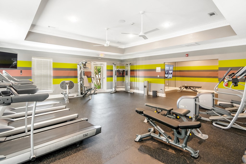 a gym with cardio equipment and weights in a building with yellow and whi at Avalon Apartments Starkville, MS