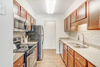 A kitchen with wooden cabinets and a black refrigerator at Cambridge Station Apartment Homes in Oxford, MS