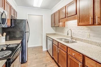 A kitchen with wooden cabinets and a black refrigerator and dishwasher at Cambridge Station Apartment Homes, Mississippi, 38655