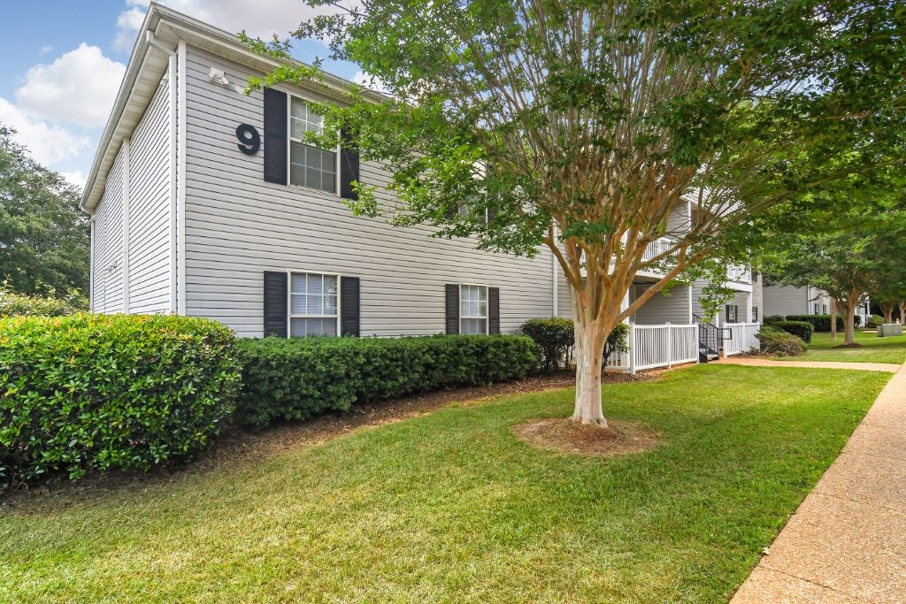 a white building with black shutters and a tree in front of it  at Parklane Apartment Homes, McComb