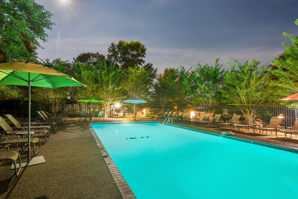 a swimming pool with chairs and umbrellas at night at Parklane Apartment Homes, McComb
