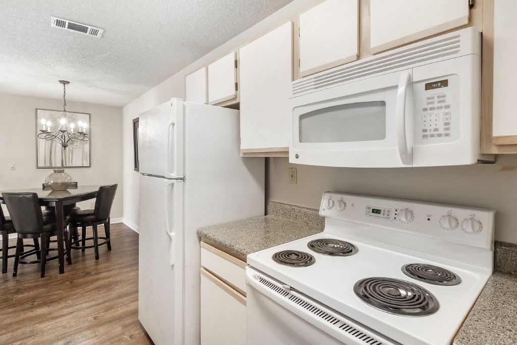 a kitchen with white appliances and a dining room in the background  at The Pointe Apartment Homes, Mississippi, 39553