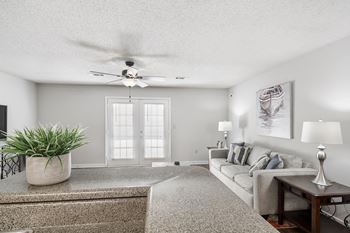 A living room with a grey couch, a plant, and a painting on the wall at The Pointe Apartment Homes in Gautier, MS
