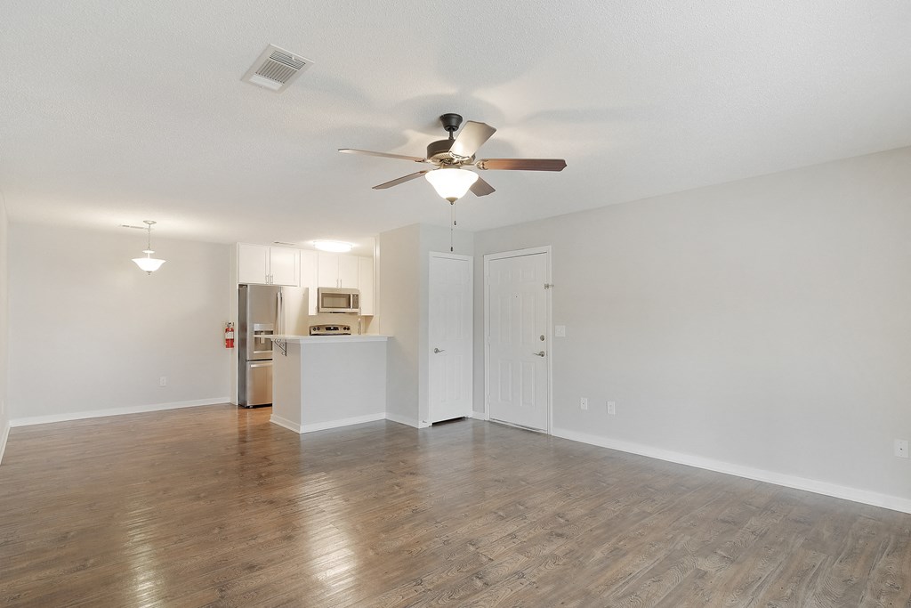an empty living room with a ceiling fan and a kitchen at The Woodlands Apartment Homes, Meridian, MS