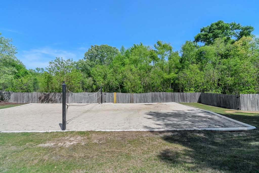 a volleyball court in a backyard with a fence and trees at Reserve of Jackson Apartment Homes, Jackson, MS