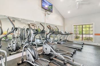 A gym with a row of stationary bikes and a television mounted on the wall at Reserve of Jackson Apartments