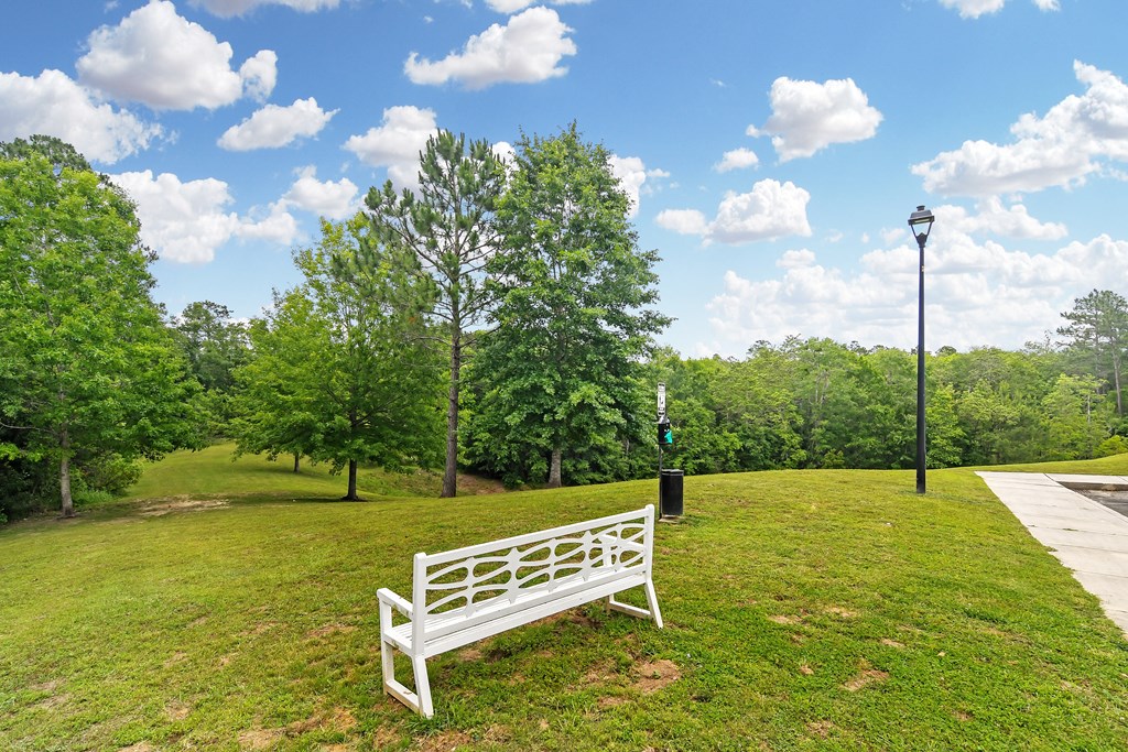 a park bench sitting in the grass next to a sidewalk at Charleston Apartment Homes, Mobile
