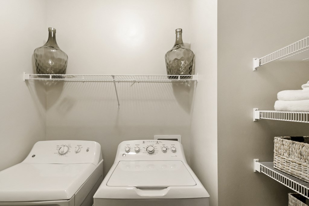 a laundry room with two white appliances and a shelf with a vase on top at Charleston Apartment Homes, Alabama