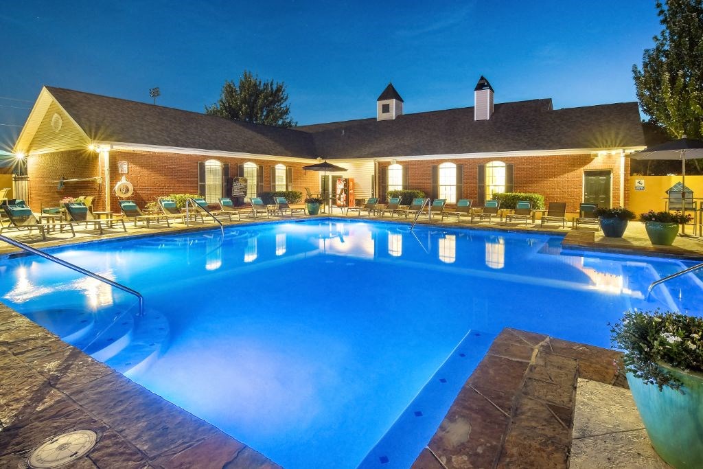 a swimming pool with lounge chairs and umbrellas at night in front of a brick building at Summit of Shreveport Apartment Homes, Shreveport, LA