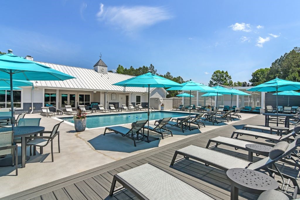 a swimming pool with chaise lounge chairs and umbrellas at The Woodlands Apartment Homes, Meridian, 39301