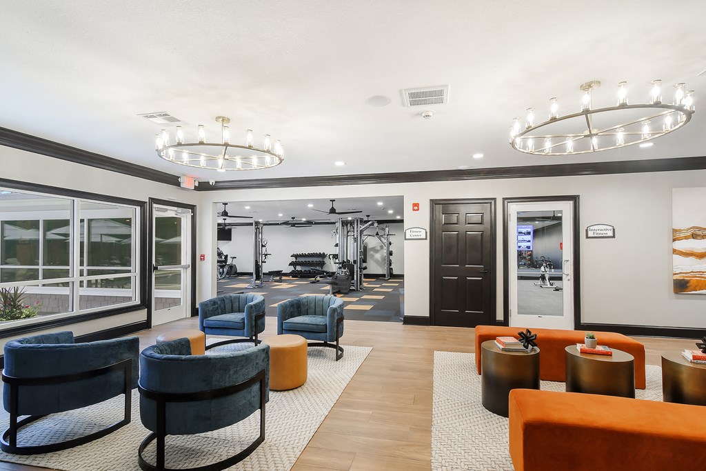 a lobby with chairs and tables and a gym in the background at The Woodlands Apartment Homes, Meridian, MS, 39301