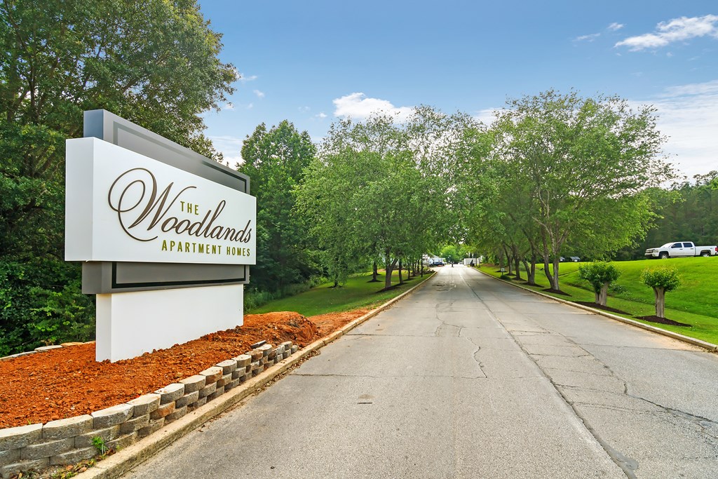 the woodlands sign at the entrance to a road with trees at The Woodlands Apartment Homes, Meridian, Mississippi